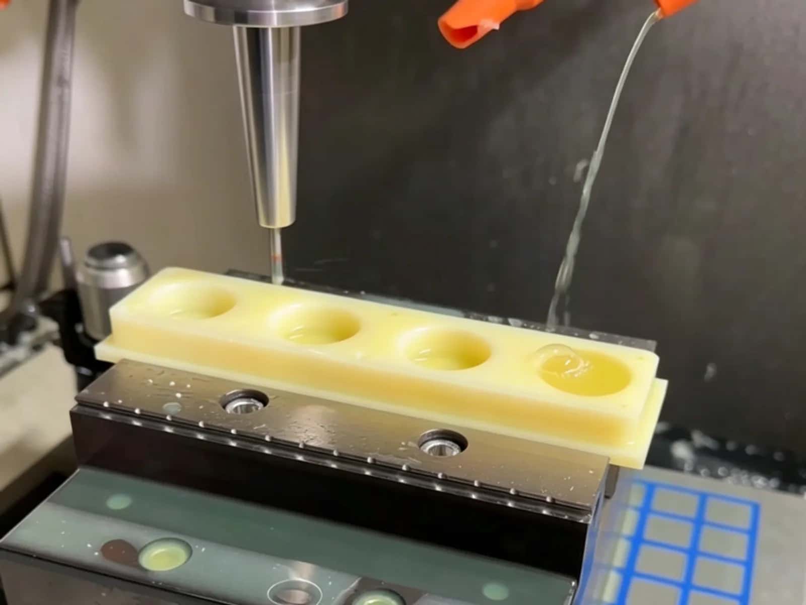 End mill cutting a yellow plastic strip with five pockets in a vise while coolant runs from Loc-Line nozzles