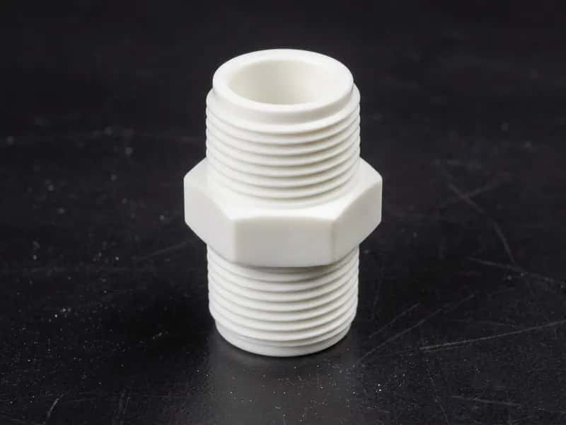 White POM hex nipple with external threads on both ends on a dark work surface