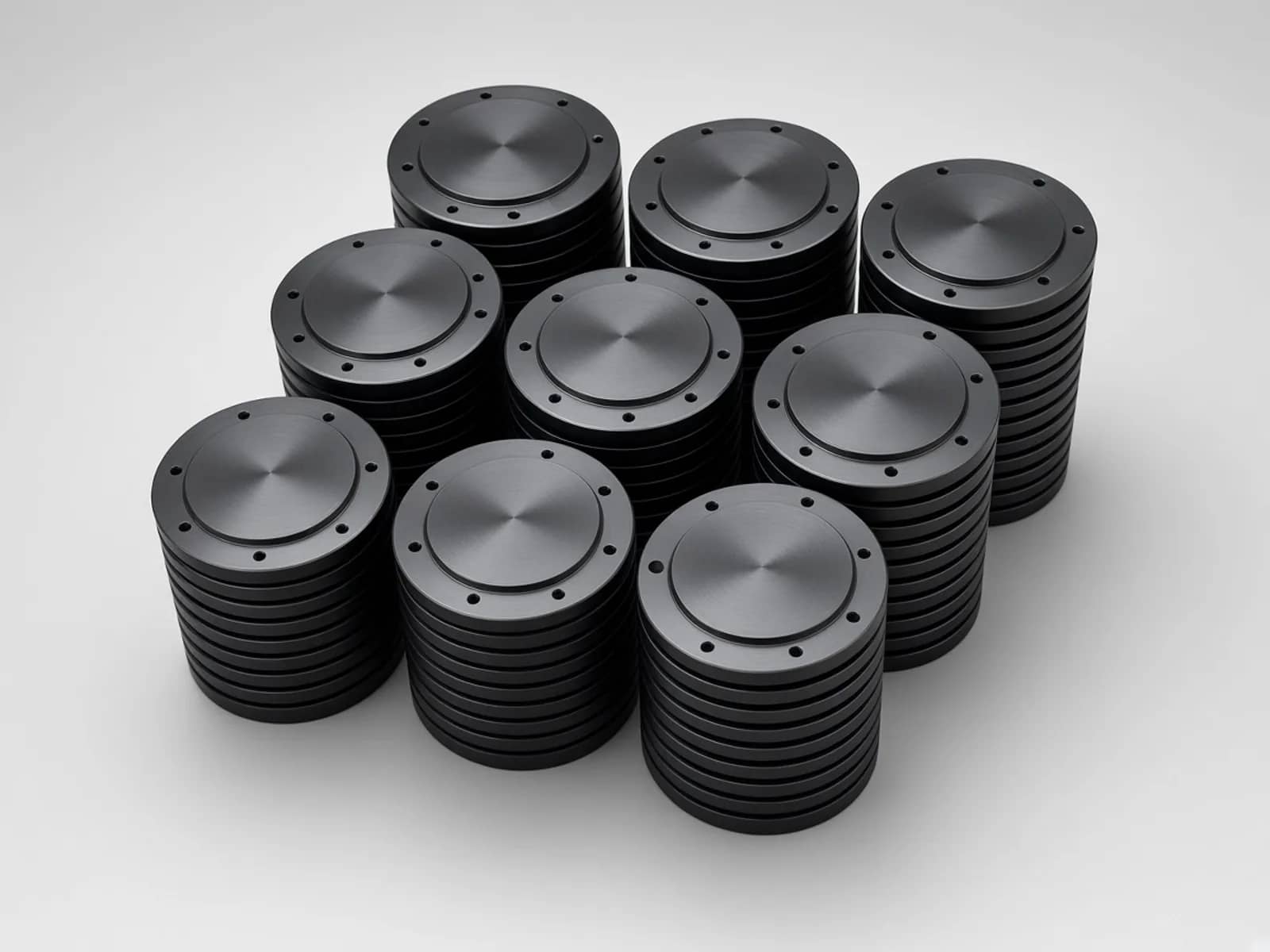 Stacks of black machined circular mounting discs with raised bosses and perimeter holes on a light gray studio surface