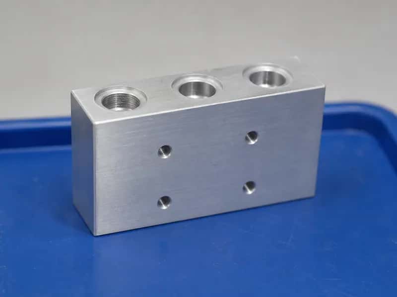 CNC milled aluminum interface block with counterbored ports and front mounting holes on a blue tray
