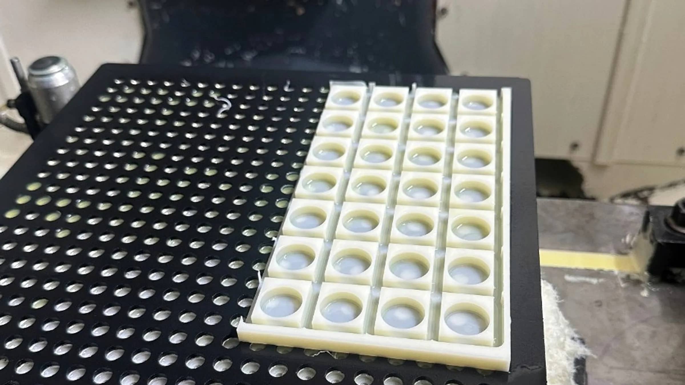 Vacuum fixture plate holding a nest tray of precision parts on a perforated suction table