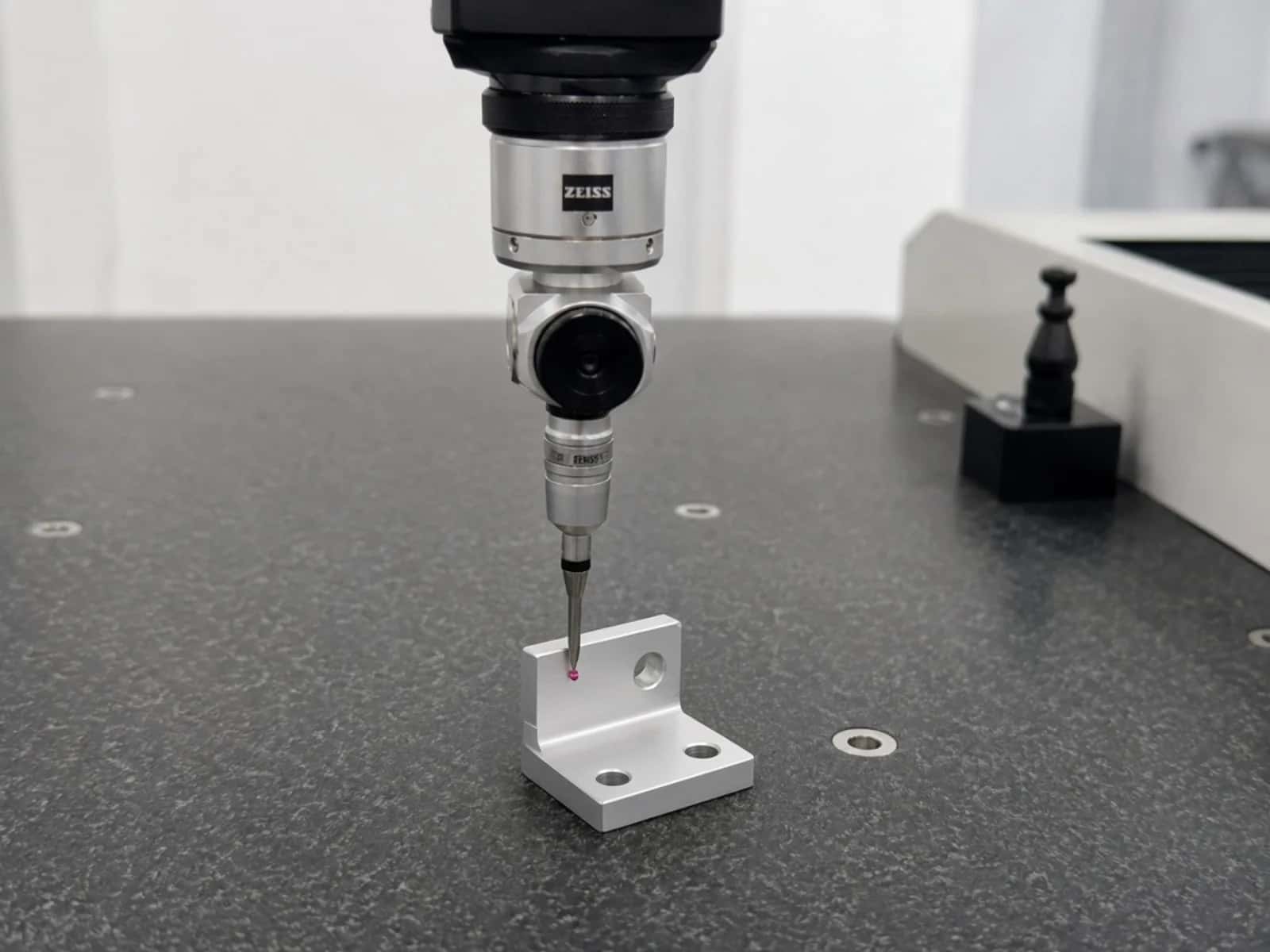 CMM probe with ruby tip measuring a simple aluminum L-bracket on a granite inspection table