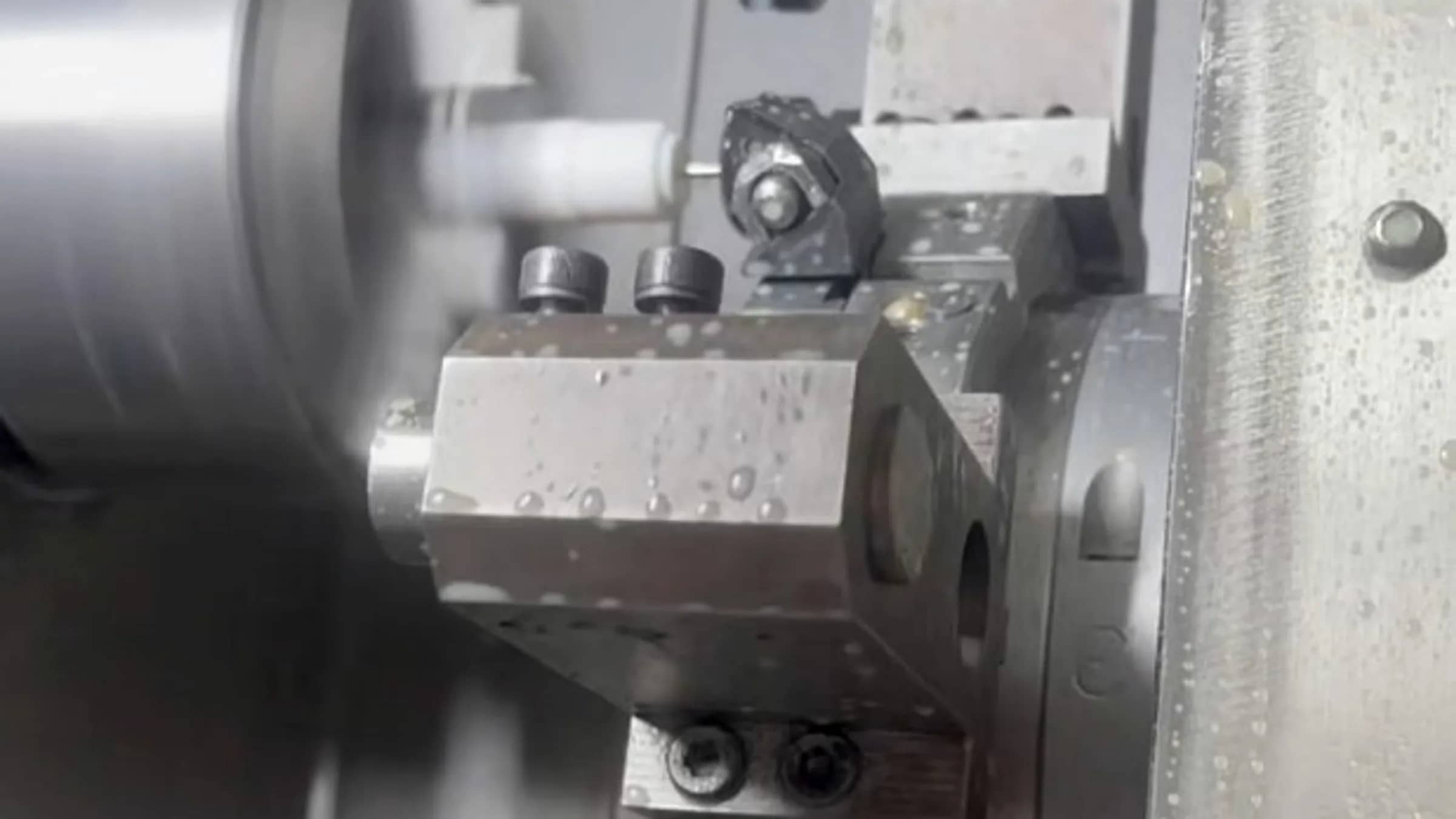 CNC turn-mill turret cutting a rotating white workpiece with coolant beads on the tooling